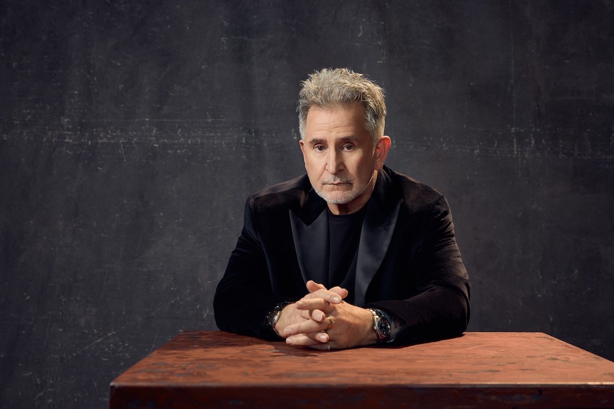 Actor Anthony LaPaglia wearing a dark jacket, sitting at a table with hands clasped in a promotional portrait for Death of a Salesman.